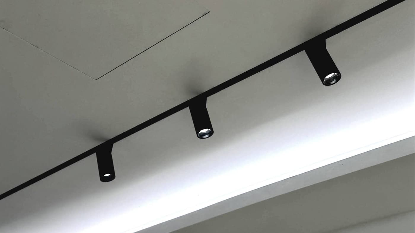 Recessed magnetic track carrying three cylindrical spot modules above a lit cove